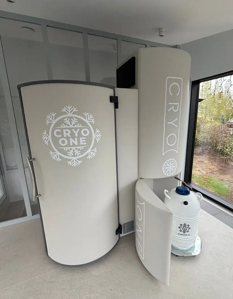 Криокапсула CryoOne Pro: кремово-белая кабина, блок агрегата и сосуд Дьюара в светлом зале с панорамным окном